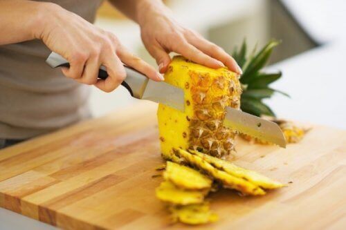 person tar bort skal på ananas med kniv