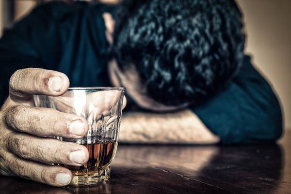 person med huvudet på bordet och glas med alkohol i handen