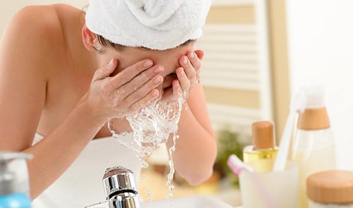 kvinna tvättar ansiktet med vatten