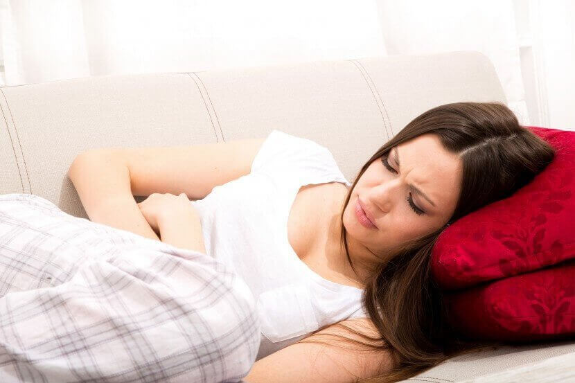 Kvinna med magont i soffan.