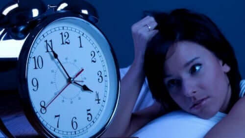 vaken kvinna i säng bredvid väckarklocka