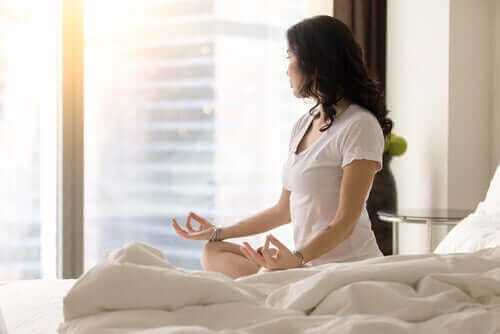 Kvinna sitter på sängen och mediterar.