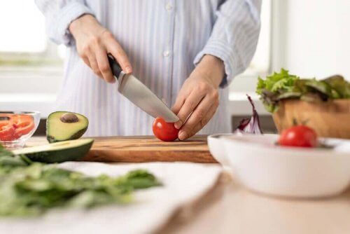 Person står i köket och skär grönsaker till en sallad.