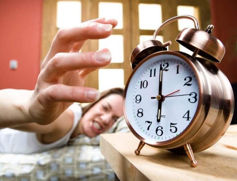 Kvinna stänger argt av sin väckarklocka på morgonen.
