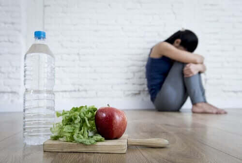 Överdriven oro för din hälsa: ihopkrupen kvinna med vattenflaska, salladsblad och äpple