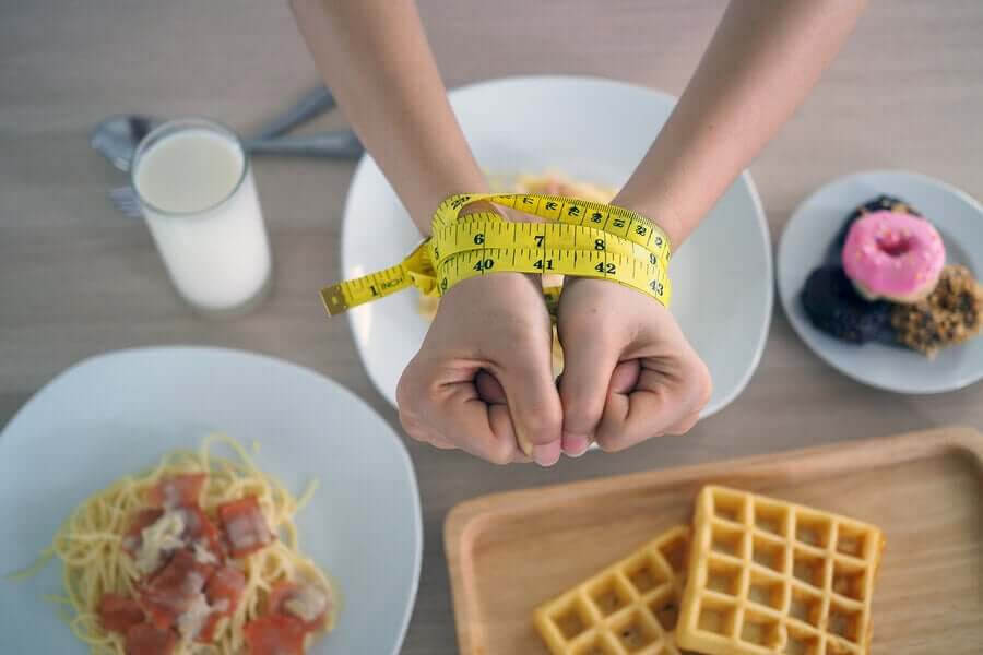  händer ihopbundna med måttband över kolhydratrik mat