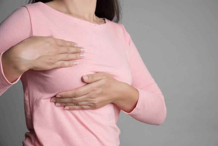 Bröstsmärta efter plastikkirurgi: kvinna undersöker sitt eget bröst