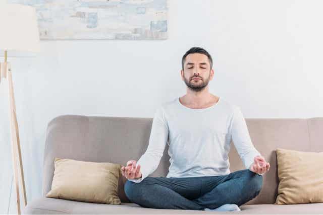 En man sitter på soffan och mediterar.