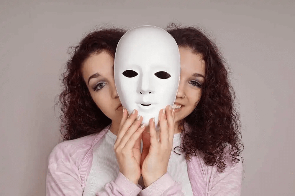 kvinna tittar fram bakom mask som ledsen och glad