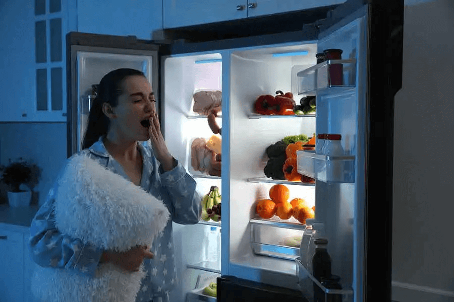 trött kvinna vid kylskåp