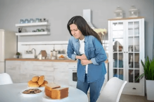 kvinna med ont i magen framför bord fullt med bröd