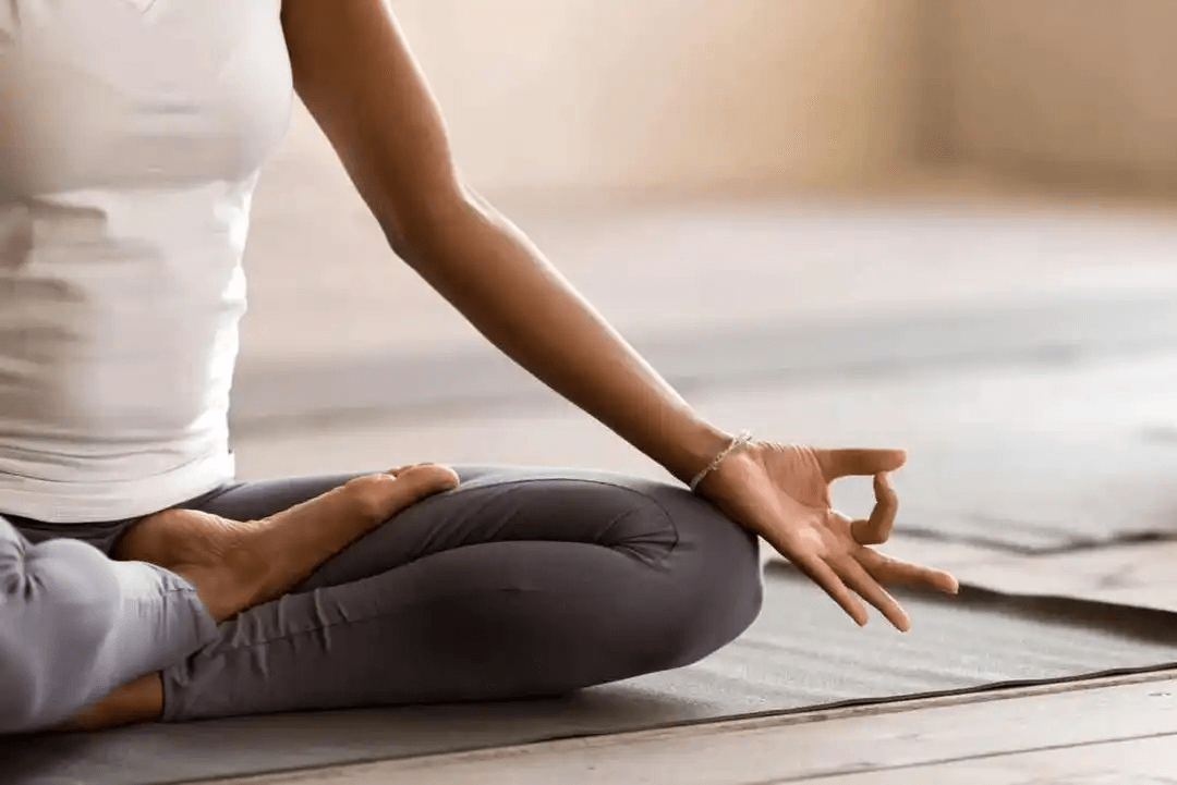 Närbild av en kvinnas hand och knän medan hon sitter på golvet och för att utöva vipassana
