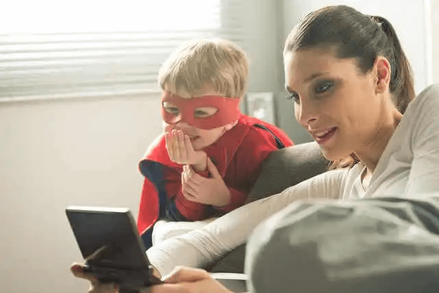 barn utklätt till superhjälte och mamma tittar på surfplatta