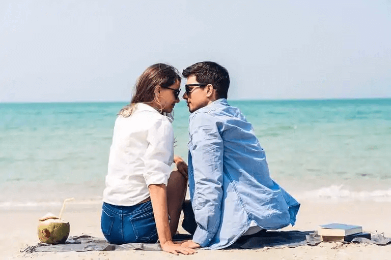 Ett par som sitter på stranden och tittar in i varandras ögon.