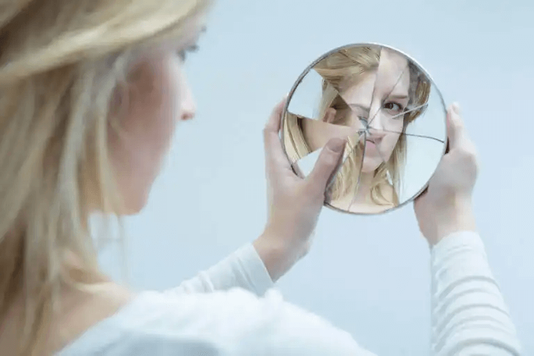 En tonårsflicka som tittar på sig själv i en trasig spegel.