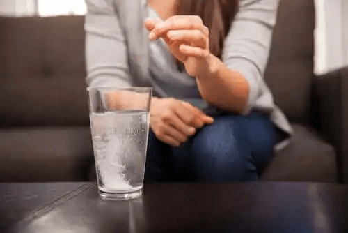 Kvinnan lägger antacida i ett glas vatten