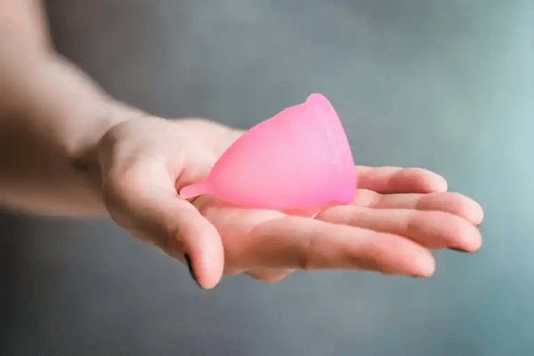 En kvinnas hand som håller en rosa menskopp.