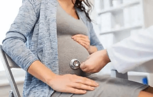 En läkare placerar ett stetoskop på en gravid kvinnas buk.