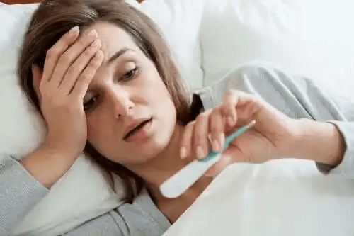En kvinna känner sin panna och tittar på en digital termometer.