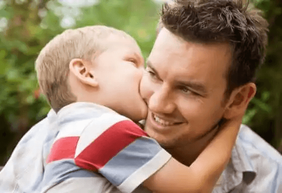 En liten pojke som kysser sin pappa på kinden.