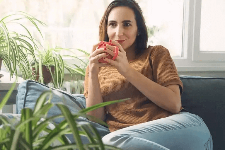 En kvinna sitter i soffan och dricker en kopp kaffe.