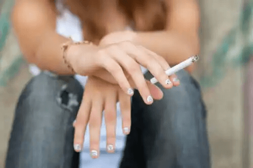En kvinna som sitter med en brinnande cigarett mellan fingrarna.