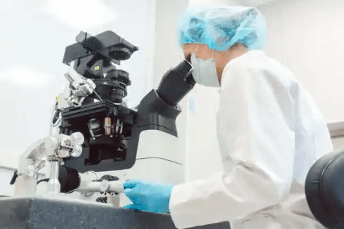 En laboratorietekniker tittar in i ett mikroskop.