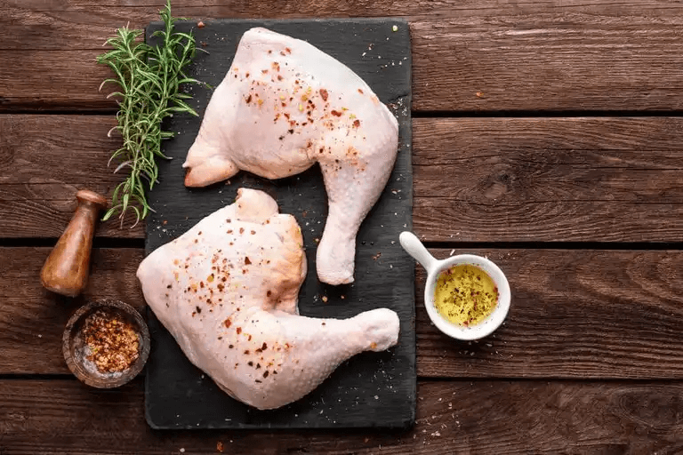 Rå kyckling på skärbräda med olivolja, kryddor och örter.