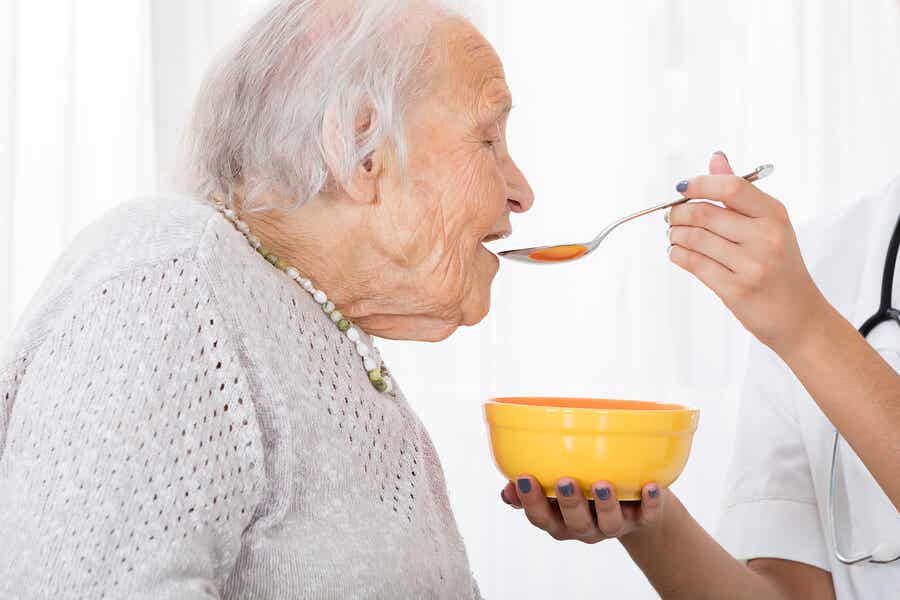 En sjuksköterska matar en äldre kvinna med en sked.