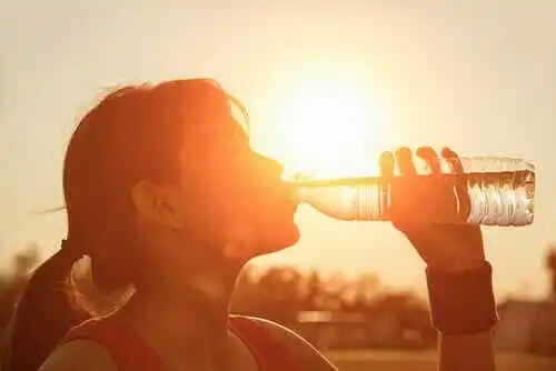 En kvinna som dricker vatten från en plastflaska en varm dag.