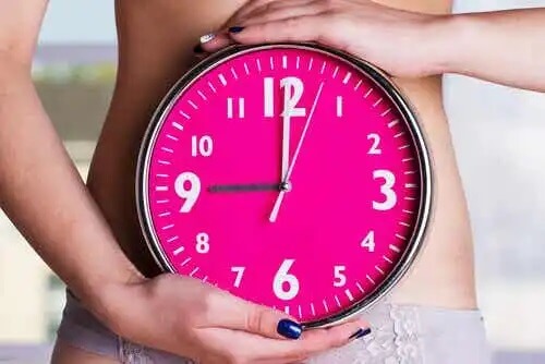 En kvinna som håller en klocka framför sin bara mage.