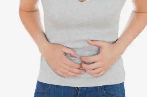 En kvinna med händerna över buken för att hon känner sig illamående.