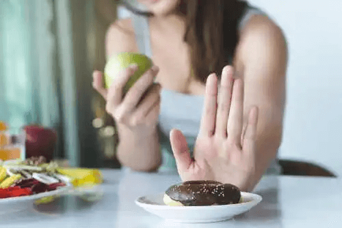 Kvinna med äpple i hand säger nej till munk för att minska socker i kosten