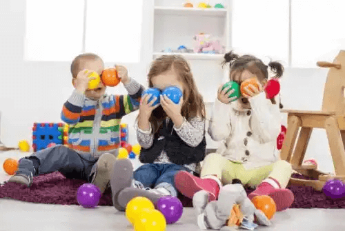 Tre barn leker med färgglada bollar