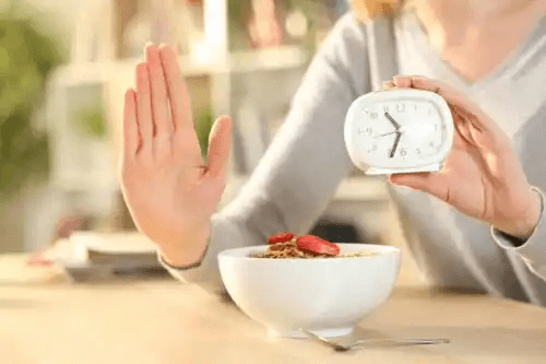 Kvinna med frukost och klocka som utövar intermittent fasta