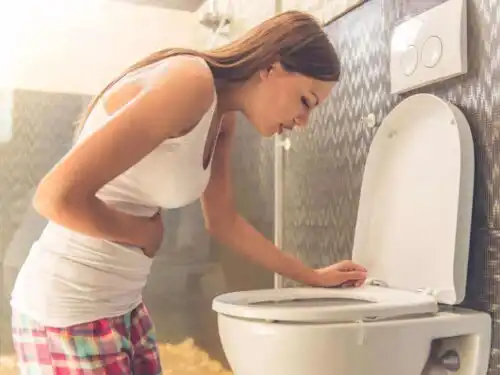 Kvinna lutar sig över toaletten vid illamående.
