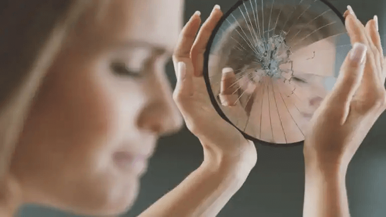 Kvinna som tittar i en trasig spegel